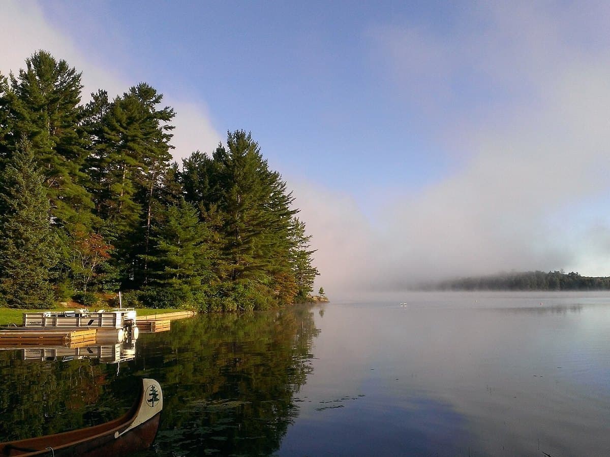 Morning mist clearing over Bark Lake, Ontario, with a canoe and dock in the foreground